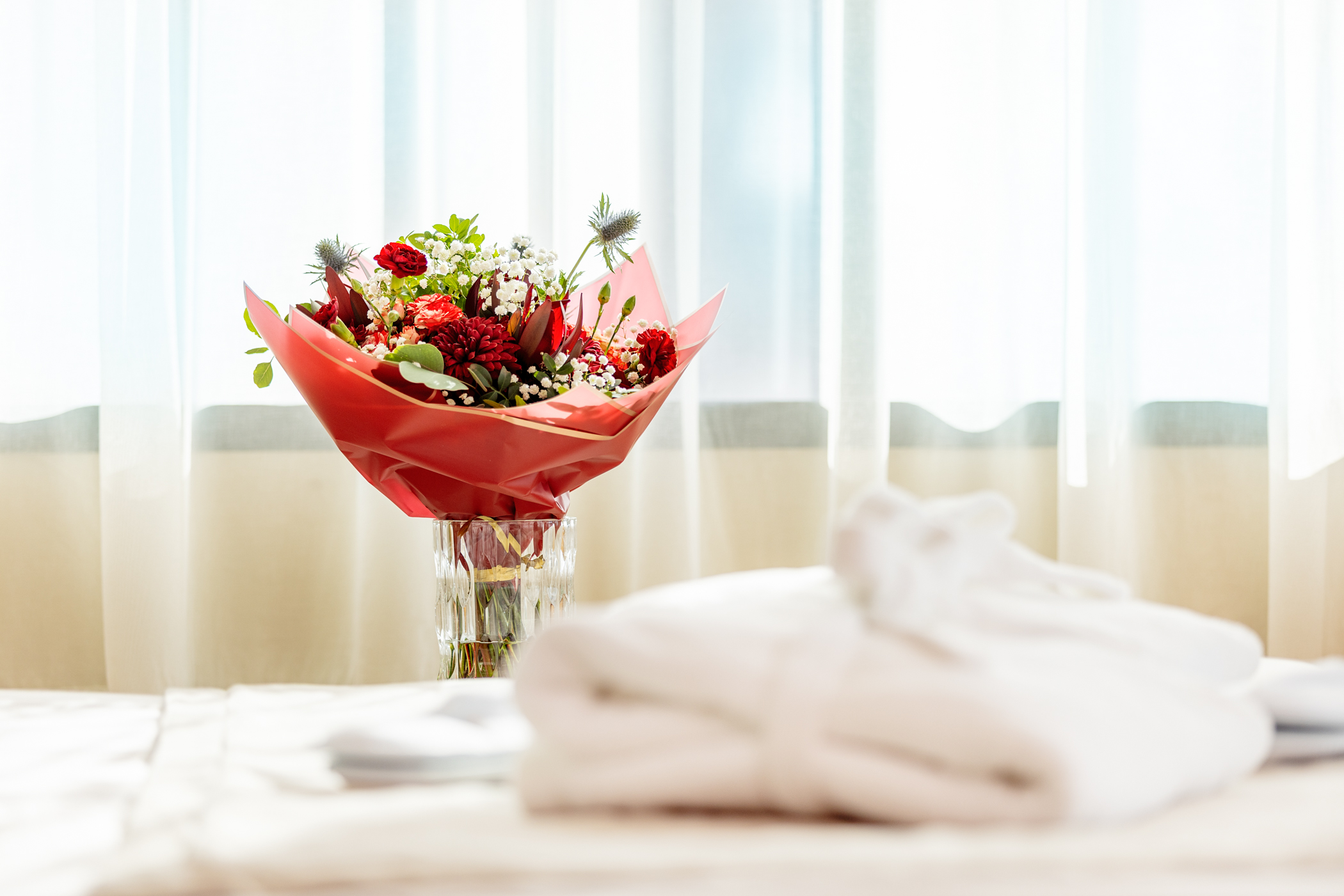 Hotell Tartu hotellitoas punane lillekimp vaasis ja hommikumantel voodil - lisateenused Tartu hotellis